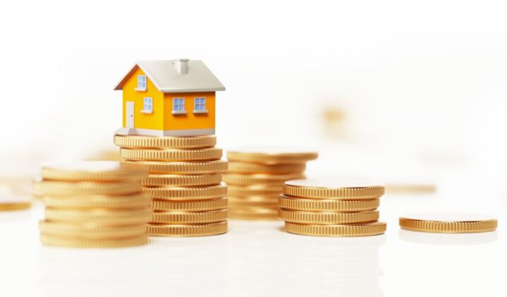 Yellow toy house is sitting on top of a coin stack. Horizontal composition with selective focus and copy space. Real Estate and Savings Concept.