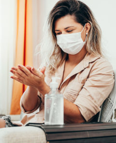 Coronavirus. Woman in quarantine wearing protective mask sanitizing her hands with alcohol gel