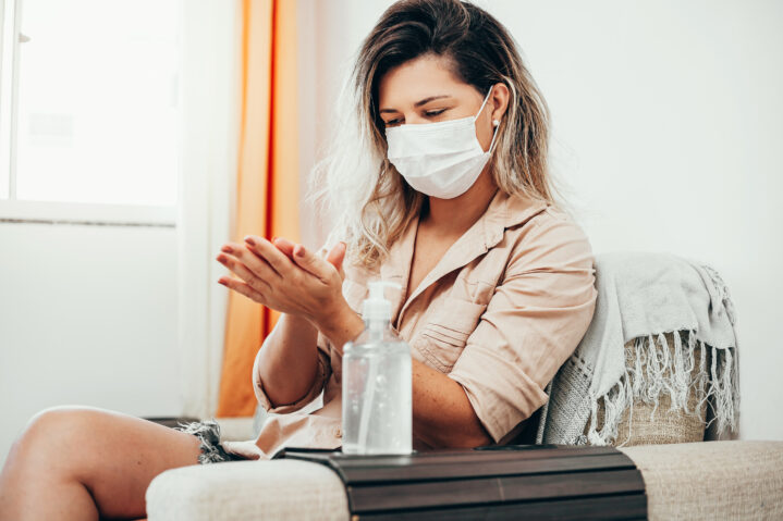 Coronavirus. Woman in quarantine wearing protective mask sanitizing her hands with alcohol gel