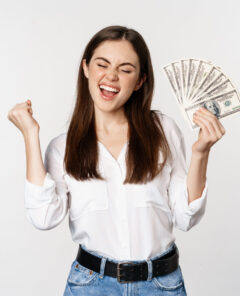 Joyful woman dancing with money, smiling pleased, winning prize, standing over white background.