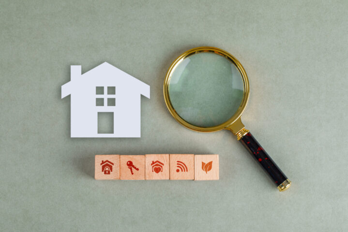 Conceptual of search real estate with wooden blocks, paper home icon and magnifying glass on sage color background flat lay. horizontal image