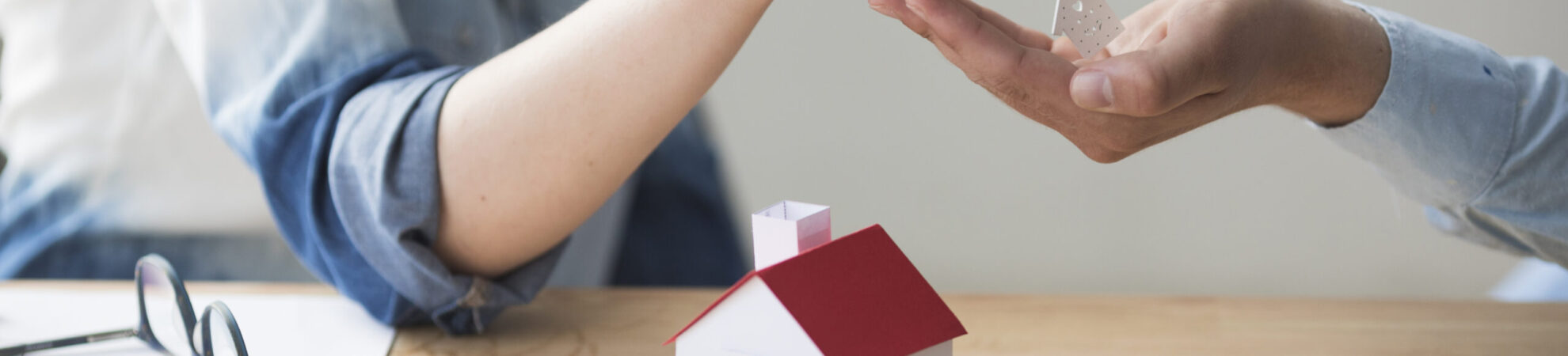 close-up-woman-s-hand-giving-house-key-man-wooden-table