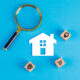 Conceptual of real estate with magnifying glass, wooden blocks, paper home icon on blue background flat lay. horizontal image