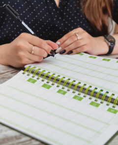 Women hands with pen write in notebook. Young girl at table in cozy office and fills out diary. Close-up of hands taking notes in magazine. Female works in an office. Planning of working time