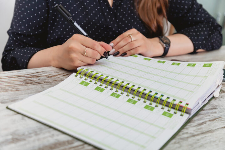Women hands with pen write in notebook. Young girl at table in cozy office and fills out diary. Close-up of hands taking notes in magazine. Female works in an office. Planning of working time