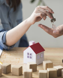 primer-plano-de-la-mano-de-la-mujer-que-da-la-llave-de-la-casa-al-hombre-sobre-mesa-de-madera