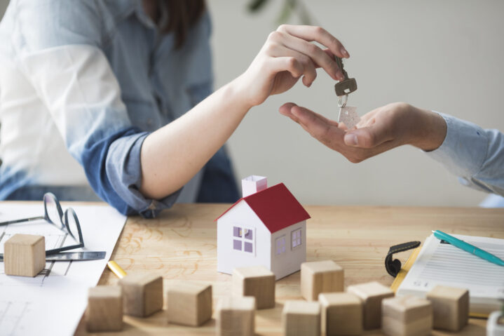 primer-plano-de-la-mano-de-la-mujer-que-da-la-llave-de-la-casa-al-hombre-sobre-mesa-de-madera